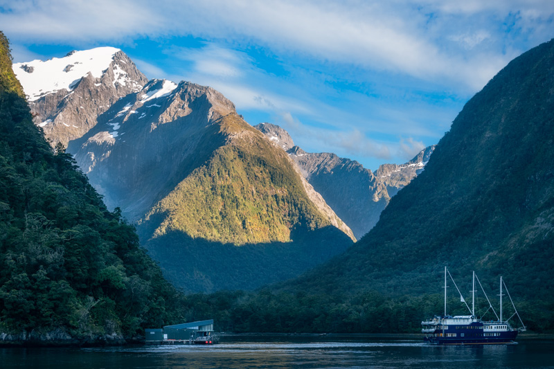 Sunny aspect early in the morning and a Cruise Boat at Harrison Cove in Milford Sound, Fiordland National Park, New Zealand, South Island.